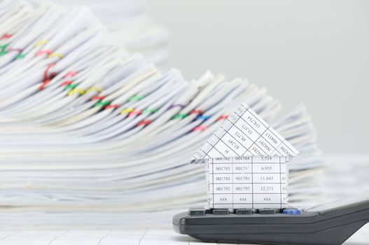 Close up house on calculator have overload of paperwork with colorful paperclip on finance account as background.