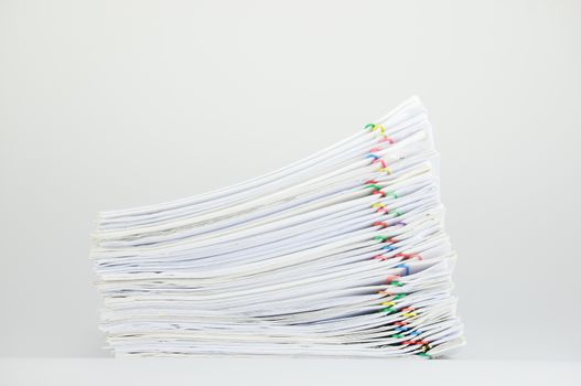Pile of paperwork with colorful paperclip on white table as background.