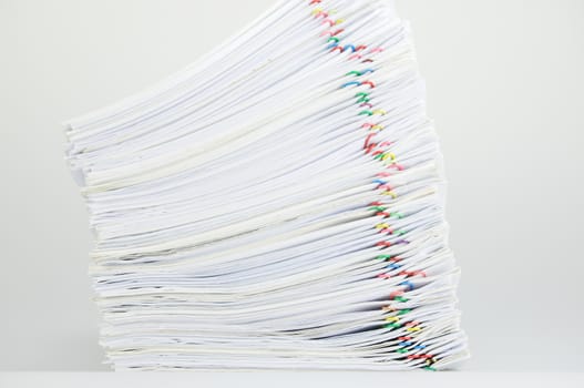 Overload pile of paperwork with colorful paperclip on white table as background.