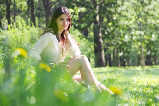 Young beautiful woman relaxing in spring park sitting under a tree