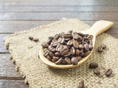Place the coffee beans in a wooden spoon on a wooden table.