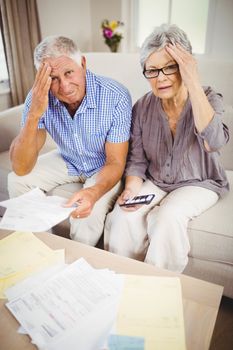 Portrait of senior couple with bills looking worried in living room