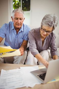 Senior woman sitting with man on sofa and paying bills online on laptop in living room