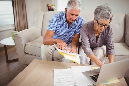 Senior woman sitting with man on sofa and paying bills online on laptop in living room