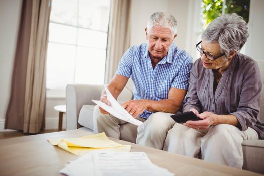 Senior man sitting with woman on sofa and showing documents in living room