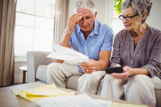 Senior man sitting with woman on sofa and showing documents in living room
