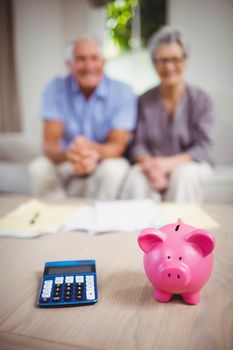 Piggy bank and calculator on table and senior couple sitting on sofa in background