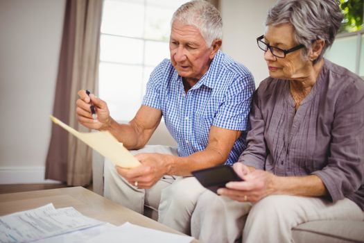 Worried senior couple sitting on sofa and calculating bills in living room