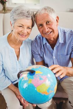 Portrait of senior couple holding a globe and smiling in living room