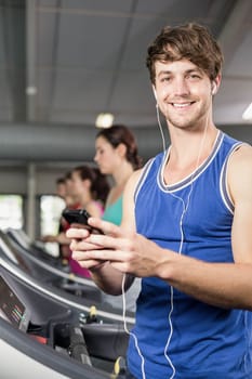 Smiling muscular man on treadmill listening to music at gym 