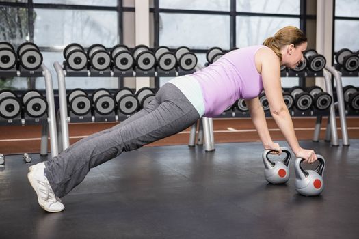 Determined woman planking with kettlebells at the gym