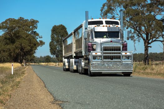 A large B-Double Semi Trailer driving down a deserted rural road.`