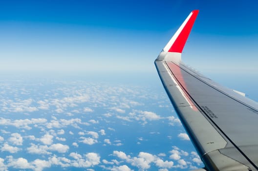 Wing of the plane on sky background - plane wing with cloud patterns - view from the window of a plane of the wing, the sky