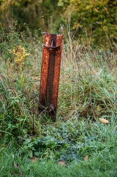 Rusty metal pole on a field with green grass