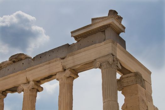 Antique ruins of a building at Acropolis in greek capital Athens. Columns and the edge of the roof. Cloudy sky in the background.