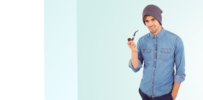 Portrait of hipster smiling while holding smoking pipe against blue background