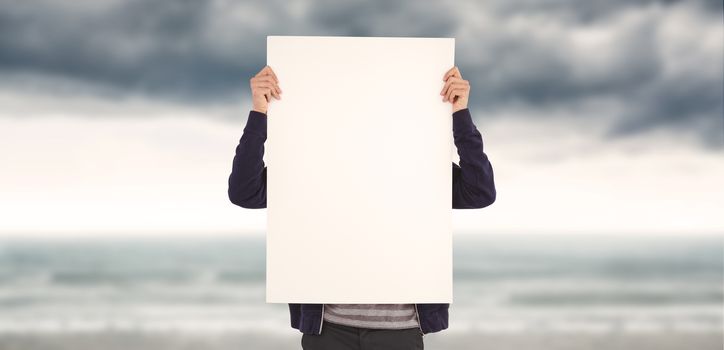 Man showing billboard in front of face against cloudy landscape background