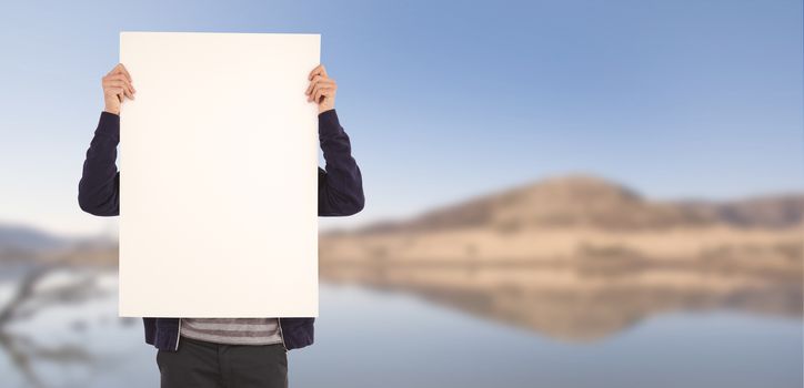 Man showing billboard in front of face against lake