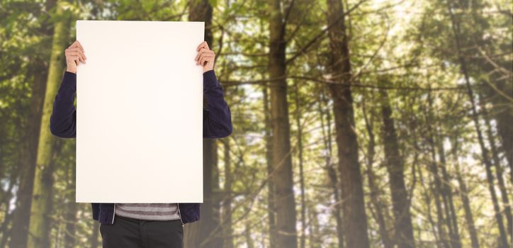 Man showing billboard in front of face against trees in a woods