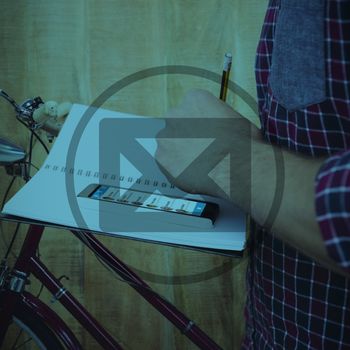 Cropped image of man with smartphone writing on book against close up view of a bicycle