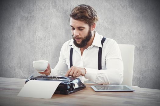 Hipster holding coffee working on typewriter against white and grey background