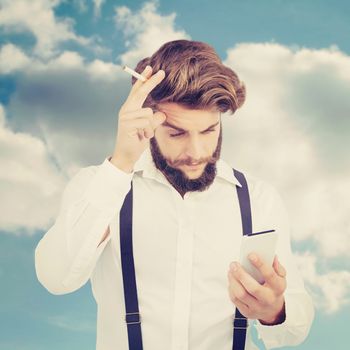 Hipster looking in mobile phonewhile holding cigarette against beautiful blue cloudy sky