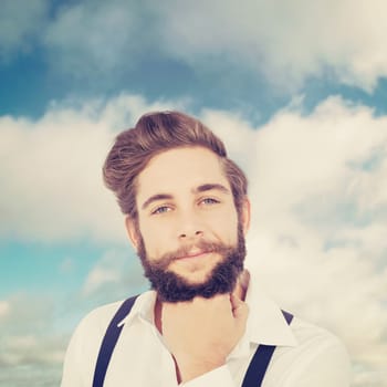 Confident hipster with hand on chin against blue sky with clouds