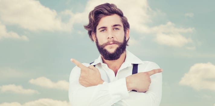 Confident hipster pointing sideways with arms crossed against beautiful blue cloudy sky