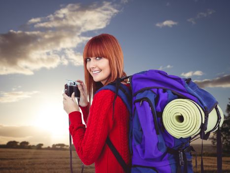 Smiling hipster woman with a travel bag against sunset over a field