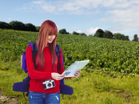Smiling hipster woman with a travel bag with a map against landscape of a field