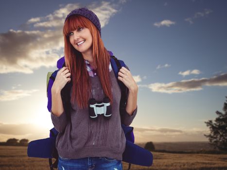 Smiling hipster woman with a travel bag against sunset over a field