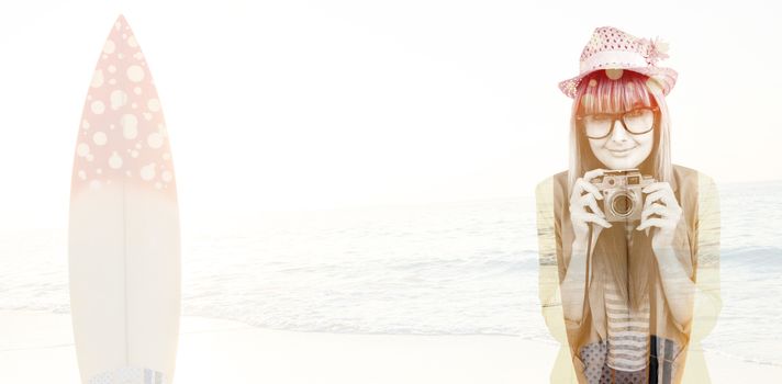 Portrait of a smiling hipster woman holding retro camera against surf board standing on the sand