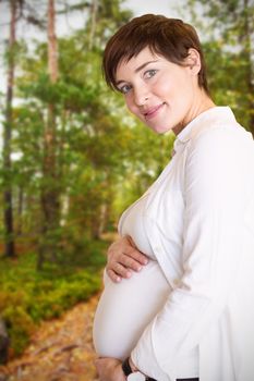Portrait of smiling pregnant woman holding belly against scenic view of walkway along lush forest