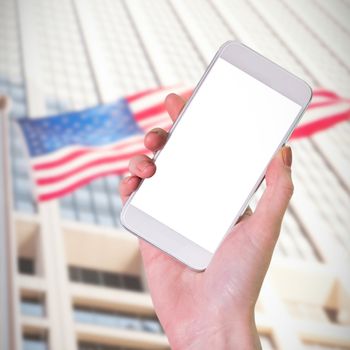 Hand holding smartphone against american flag against sky scraper