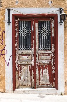 Old entrance door to the house with dark red peeled of painting. White frame. Yellow facade. Lantern to enlighten the door.