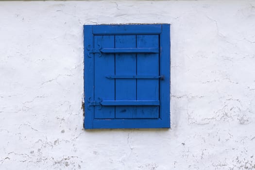 Horizontal front view of a blue window with closed wooden blind on a white textured building wall