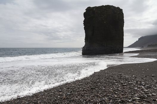 Horizontal view of an Icelandic beach with a huge rock formation in the middle