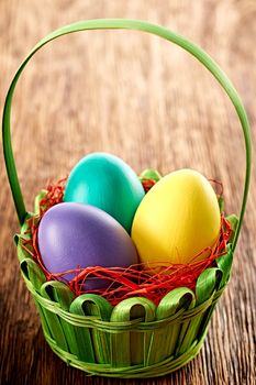 Easter eggs in green basket. Hand painted decorated multicolored eggs on wooden background. Unusual creative holiday greeting card 