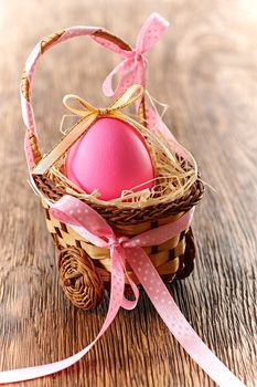 Easter egg in basket. Hand painted decorated pink egg with bow on wooden background. Unusual creative holiday greeting card 