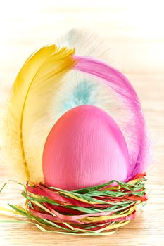 Easter egg in nest. HHand painted decorated egg with and feathers on wooden background. Unusual creative holiday greeting card 