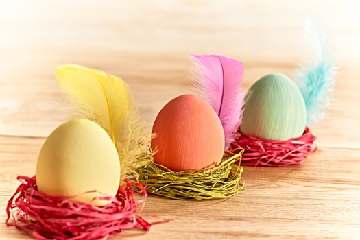Easter eggs in nests. Hand painted decorated multicolored eggs with feathers on wooden background. Unusual creative holiday greeting card 