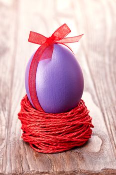 Easter egg in nest. Hand painted decorated egg with bow on wooden background. Unusual creative holiday greeting card 