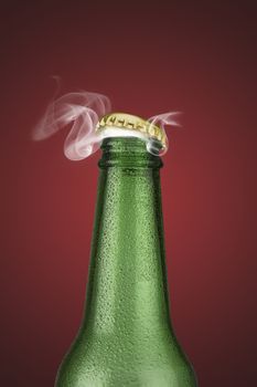 Green cold beer bottle with water drops and golden cap open on red background