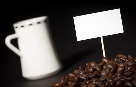 A pile of coffee beans with an empty sign on top of them and a white coffee cup in the background 