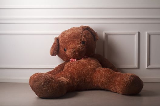 Huge toy bear with a dotted bow standing on the floor against the white wall of an empty room