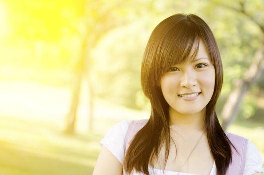 Portrait of young Asian college student standing on campus lawn, with backpack and smiling.