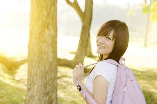 Young Asian university student standing on campus lawn, with backpack and smiling.