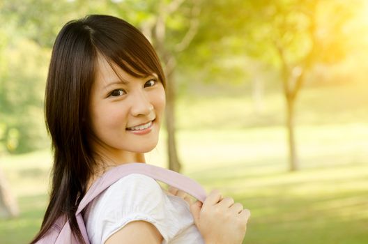 Young Asian adult student standing on campus lawn, with backpack and smiling.