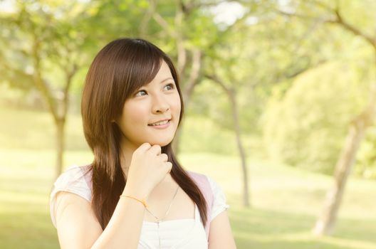 Young Asian college girl student standing on campus lawn, thinking and smiling.