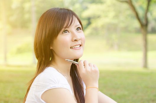 Young Asian college girl student sitting on campus lawn and thinking.